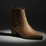 Bota texana de caña media color tostado, con puntera fina y taco cuadrado. Presenta detalles de costuras decorativas en el empeine y apliques de tachas metálicas pequeñas en los laterales y el talón.
