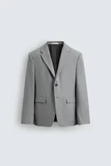 Blazer slim fit de color gris, con cuello de solapas de muesca, cierre frontal de dos botones, bolsillos laterales con solapa y bolsillo de vivo en el pecho. Presenta mangas largas con botones en los puños y aberturas en la espalda.