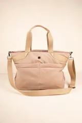 Bolso tipo shopper color beige, con asas fijas superiores y correa desmontable y regulable. Cuenta con dos bolsillos externos y tres bolsillos internos.