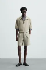 Bermuda de hombre color verde claro, de corte regular y tiro medio, con pinzas frontales, bolsillos laterales y bolsillos traseros de vivo. Cierre frontal con botón y cremallera.