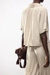 Camisa negra de cuello solapa con escote pico y manga corta. Detalle de nido de abeja en espalda. Cierre frontal con botones.