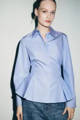 Camisa de algodón con cuello solapa, manga larga con puños y diseño peplum en el bajo. Presenta cierre frontal con botones ocultos por solapa.