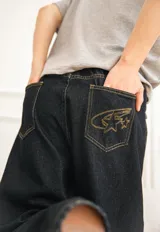 Jeans baggy de denim color azul oscuro, de corte ancho y relajado, con cintura semi-elástica en la parte trasera. Presenta bolsillos traseros con costuras a contratono y bordado de estrella en uno de ellos.