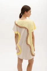 Vestido corto de algodón con diseño de bloques de color en tonos azul y celeste. Presenta un corte relajado, cuello redondo, mangas cortas y detalles de volados aplicados en forma curva a lo largo de la prenda.