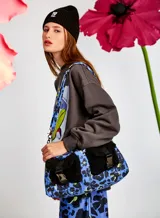 Bolso puffer chico capitoneado con estampado animal print en tonos azul y negro, con bolsillos de sherpa negros y correa desmontable con estampado a juego.