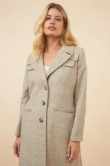 Tapado largo de corte recto confeccionado en lana fina sin teñir. Presenta cuello solapa, cierre frontal con botones, bolsillos laterales con tapa y detalles aplicados en la parte delantera. Incluye forro interior y tajo en la espalda.