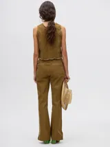 Pantalón de denim color marrón, de tiro alto y calce ochentoso con terminación estilo oxford. Cuenta con apliques metálicos decorativos alrededor de los bolsillos y a lo largo de las costuras exteriores.
