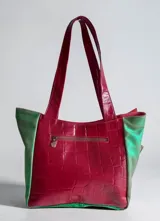 Cartera tipo tote de cuero combinada con diseño patchwork en tonos verde, bordó, beige y detalles metalizados, con doble asa de hombro y cierre superior.
