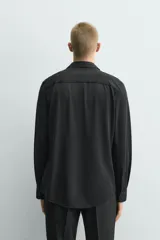 Camisa de manga larga color verde oscuro, con cuello italiano abierto y cierre frontal de botonadura. Presenta un calce ajustado (slim fit) y puños con botón.
