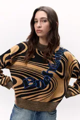 Sweater tejido de punto con diseño marmoleado en tonos ocre y negro, con aplique bordado en azul. Tiene cuello alto dorado, mangas largas abullonadas y corte holgado.