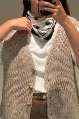 Chaleco tejido de punto con hilo lurex en color crudo, con escote en V y cierre frontal de botones jaspeados.