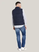Chaleco acolchado de nailon en color azul marino, con cuello alto, cierre frontal de cremallera con detalles distintivos de la marca y bolsillos laterales con cierre. Presenta el logo de Tommy Hilfiger bordado en el pecho.