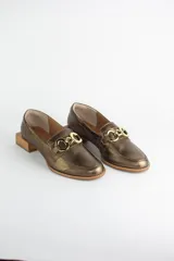 Mocasines de cuero en tono bronce metalizado, con detalle de aplique metálico dorado en el empeine y taco cuadrado bajo de madera.