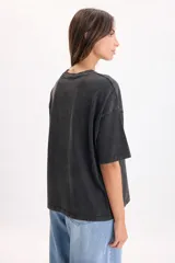 Camiseta boxy de manga corta color gris oscuro con efecto gastado, cuello redondo y estampa frontal que incluye un tigre rodeado de rosas y la frase "Only the strong survive".