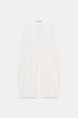 Pantalón blanco de tiro medio, pierna ancha y largo cropped. Presenta pliegues marcados en el delantero y cierre frontal con cremallera, botón y ganchos metálicos.