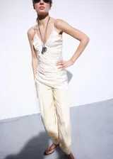 Vestido corto de tejido satinado en color beige, con diseño entallado, fruncidos ajustables laterales, escote de pico y tirantes finos.