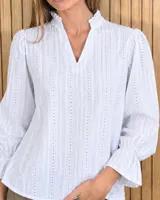Blusa rosada de algodón con delicados bordados florales blancos, escote en V con cuello elevado y volados, y mangas largas con puños acampanados.