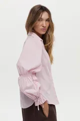 Camisa blanca de manga larga abullonada con detalle de punto smock en los puños y cordones para atar. Presenta cuello clásico y cierre frontal de botones.
