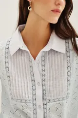 Camisa de algodón con diseño de encaje bordado, cuello clásico y frente con tablas verticales. Presenta mangas largas con puños abotonados y cierre frontal con botones.