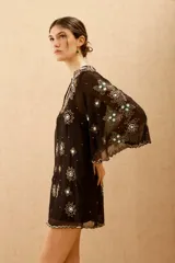 Vestido corto negro de tela transparente con mangas acampanadas y escote en V. Está completamente bordado con motivos florales y estrellas en lentejuelas y cuentas plateadas y verdes.