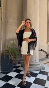 Vestido largo de tejido de red blanco, con apliques de flores negras en relieve. Lleva tirantes finos y tiene un corte recto con abertura lateral. Se usa sobre una prenda interior blanca.