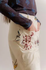 Pantalón de gabardina color crudo con estampado artístico de motivos botánicos y arquitectónicos. Presenta corte recto, tiro medio y bolsillos laterales.