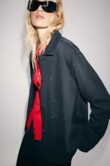 Chaqueta oversize de mezclilla color azul marino, de cuello solapa y manga larga, con bolsillos de parche en el delantero y cierre frontal con botones metálicos.
