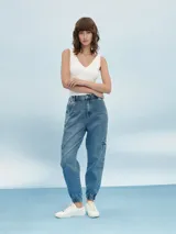 Pantalón jean de corte relaxed, con diseño cargo, cintura elástica con cordón ajustable y puños elastizados en los tobillos. Presenta bolsillos laterales en las piernas y bolsillos traseros.