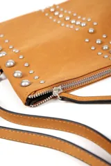 Cartera marrón con solapa frontal decorada con tachas plateadas de diferentes tamaños. Cuenta con un cierre de cremallera en la parte superior y una correa ajustable para llevar al hombro.