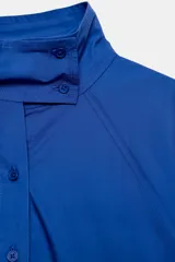 Camisa amplia blanca de cuello alto y manga larga, con cierre frontal de botones.
