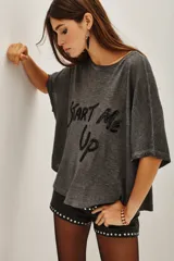 Remera de corte holgado y mangas cortas, confeccionada en tejido gris con efecto lavado. Presenta una estampa frontal con la frase 'Start Me Up' realizada en lentejuelas negras.