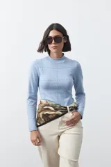 Polera de tejido de punto color celeste, con cuello alto y textura de pequeños puntos en relieve formando una cuadrícula en el frente y las mangas. De corte ajustado y manga larga.