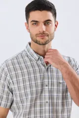 Camisa de manga corta confeccionada en mezcla de lino y algodón, con diseño a cuadros en tonos gris, blanco y azul. Presenta cuello camisero con botones y bolsillo ojal en el pecho con detalle bordado.