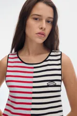 Vestido midi de punto sin mangas con diseño de rayas, corte evasé. Presenta un diseño bicolor asimétrico: el lado izquierdo con rayas horizontales blancas y rojas sobre fondo celeste, y el lado derecho con rayas horizontales negras y blancas. Incluye un pequeño parche bordado en el pecho.