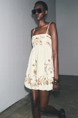 Vestido corto color crudo con tirantes finos ajustables, escote recto y bordado floral a contraste.