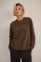 Sweater de cuello redondo y manga larga en color marrón chocolate. Presenta un bordado frontal exclusivo con tres iconos: un mate, un sol y un caballo. De calce relajado y diseño oversize.