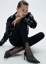 Cardigan negro de punto con cuello en pico y cierre frontal de botones. Presenta un diseño corto con mangas largas y puños elásticos, decorado íntegramente con lentejuelas circulares brillantes.