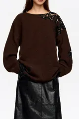 Jersey de punto color marrón con detalles de encaje negro aplicados en el hombro y lateral. Presenta cuello redondo, manga larga y corte holgado.