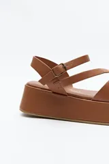 Sandalia negra con plataforma, tiras cruzadas sobre el empeine y pulsera ajustable al tobillo.