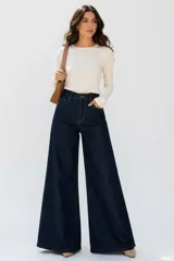Jeans oxford de mezclilla azul oscuro, tiro alto, con bolsillos laterales y traseros, y perneras amplias y acampanadas.