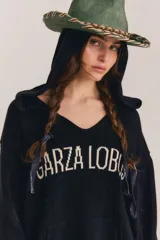 Sweater de punto negro con capucha y cuello en V, de manga larga y diseño holgado. Cuenta con el nombre de la marca bordado en el frente en color blanco, bolsillo estilo canguro, y detalles de rayas blancas en contraste en los puños y el ruedo.