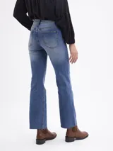 Jean de corte bootcut en color azul medio, con diseño de cinco bolsillos, cierre frontal con botón y cremallera, y bajo con terminación al corte.