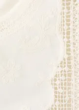 Top blanco de algodón con cuello redondo, detalles bordados, inserciones de encaje y terminaciones festoneadas en mangas y ruedo.