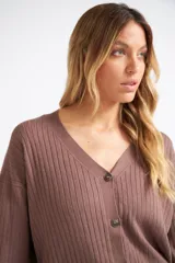 Cárdigan de tejido liviano con textura acanalada, cuello en V y cierre frontal con botones. Presenta mangas largas y un diseño clásico con detalle de grifa en cuero.