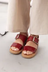 Sandalias de cuero marrón, con diseño de dos fajas amplias, una lisa en la parte delantera y otra superior con hebilla metálica grande y ajustable. Suela plana con plataforma baja y pespunte visible.