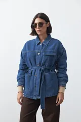 Sobrecamisa de jean color negro con silueta relajada, cuello camisero, cierre frontal con botones metálicos, bolsillos frontales y cinturón ajustable en la cintura.