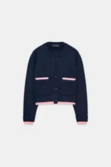 Chaqueta de punto de cuello redondo y manga larga, con cierre frontal de botones. Presenta dos bolsillos delanteros de plastrón y detalles de ribetes en color rosa a contraste en los puños, el ruedo y los bolsillos.
