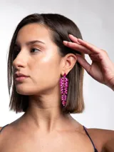 Aros colgantes largos de fiesta con diseño de hojas o pétalos encadenados en color fucsia, con cristales facetados y base metálica dorada.