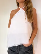 Top halter blanco de lino, con escote cruzado, detalles fruncidos en los bordes y flecos decorativos en el ruedo.