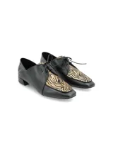 Zapato de estilo masculino color negro, confeccionado en cuero con detalles en estampa animal print de cebra, con cordones y taco bajo cuadrado.